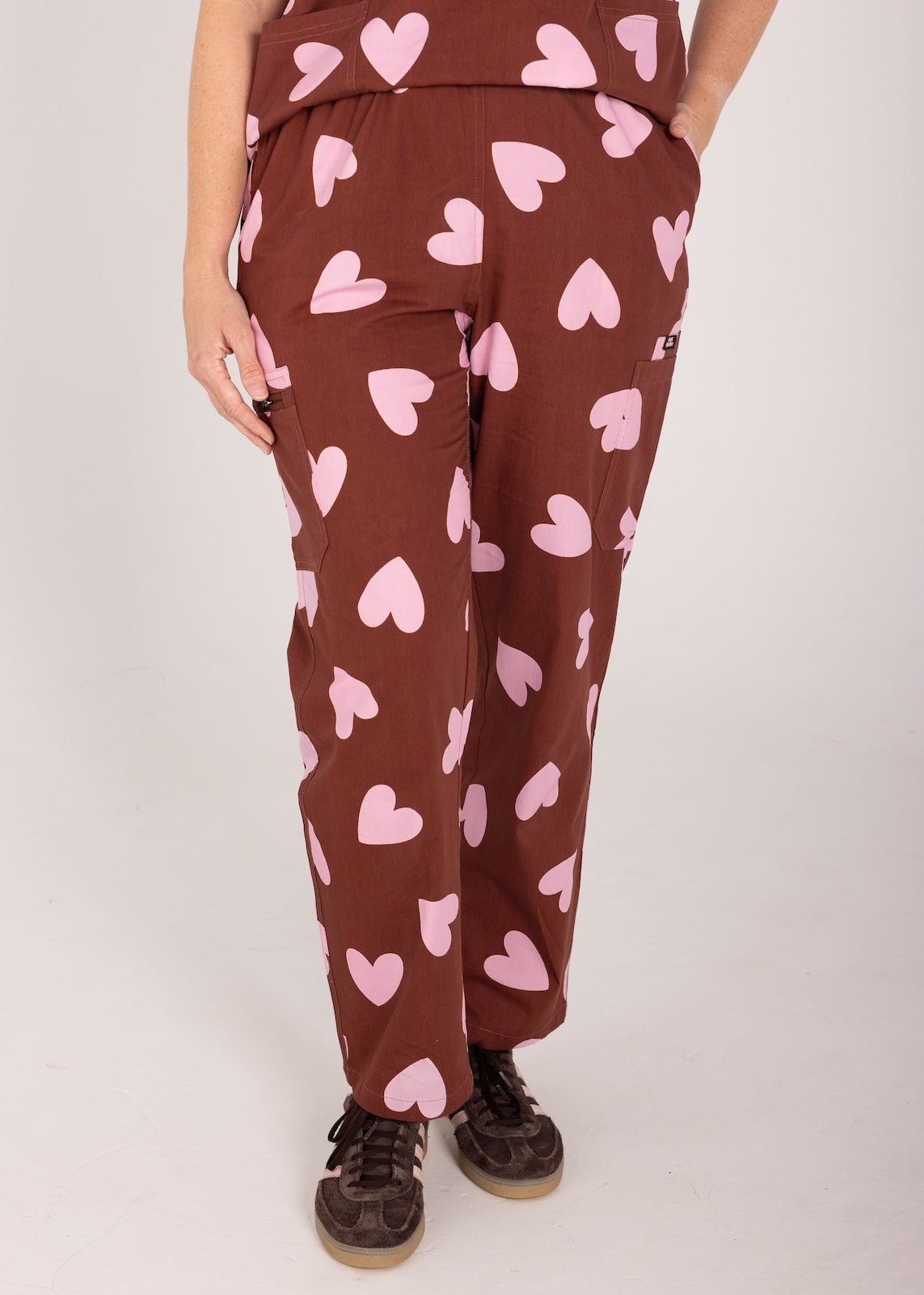 Woman wearing a brown fun scrubs with pink heart patterns on a plain background