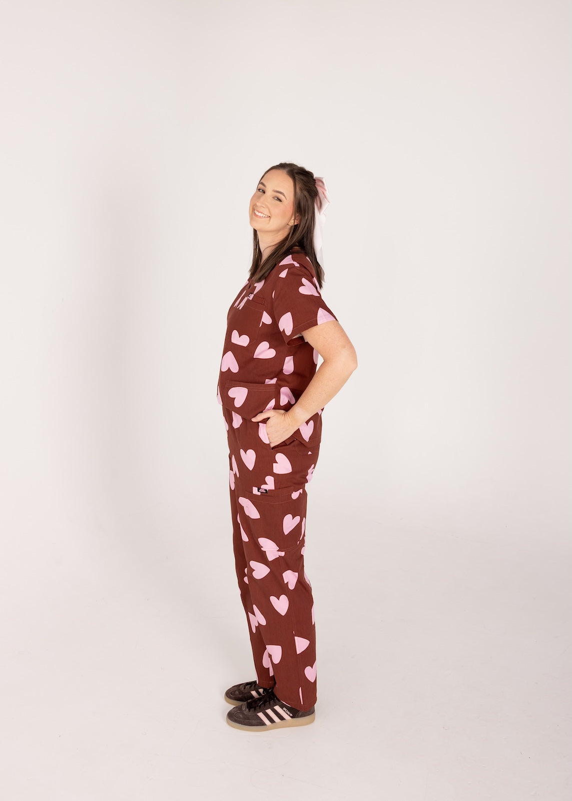 Woman wearing a brown fun scrubs with pink heart patterns on a plain background