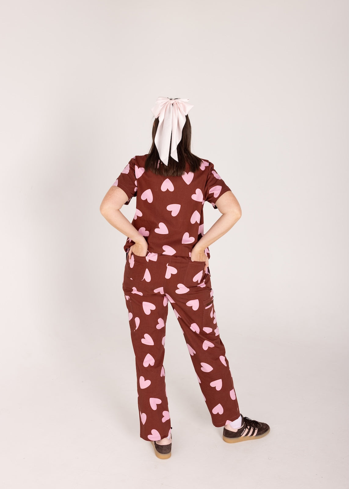 Woman wearing a brown fun scrubs with pink heart patterns on a plain background