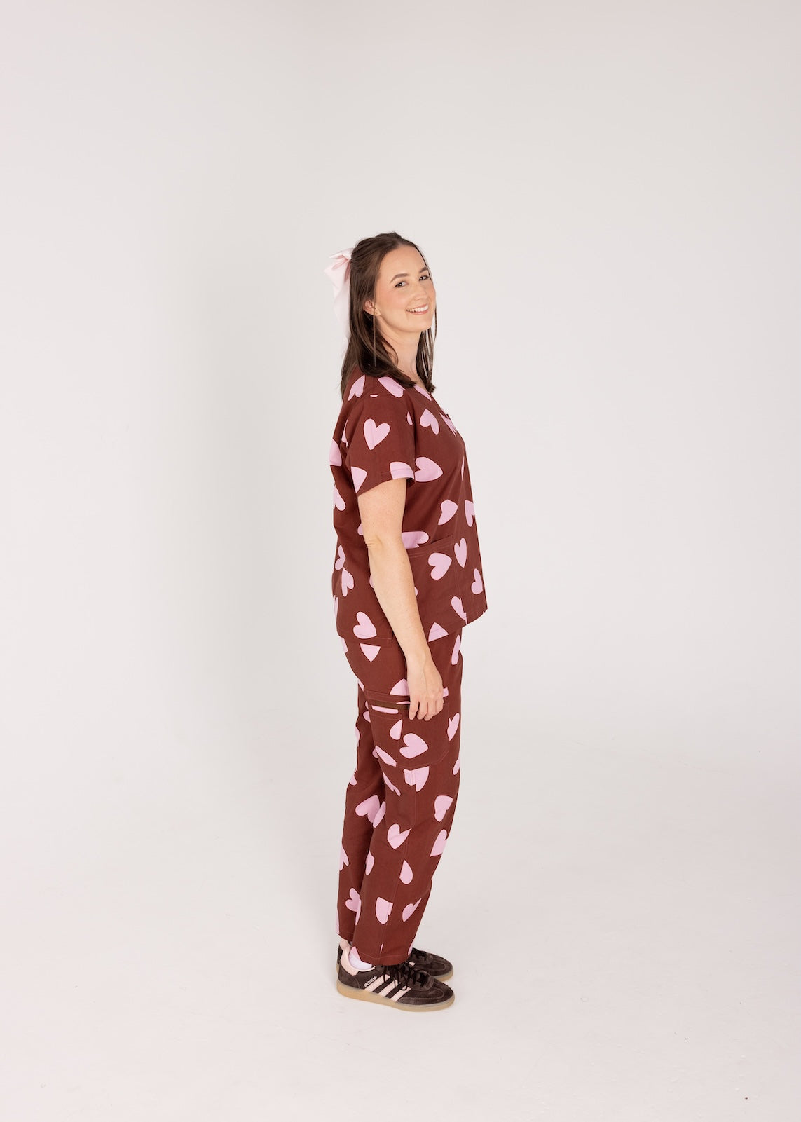 Woman wearing a brown fun scrubs with pink heart patterns on a plain background