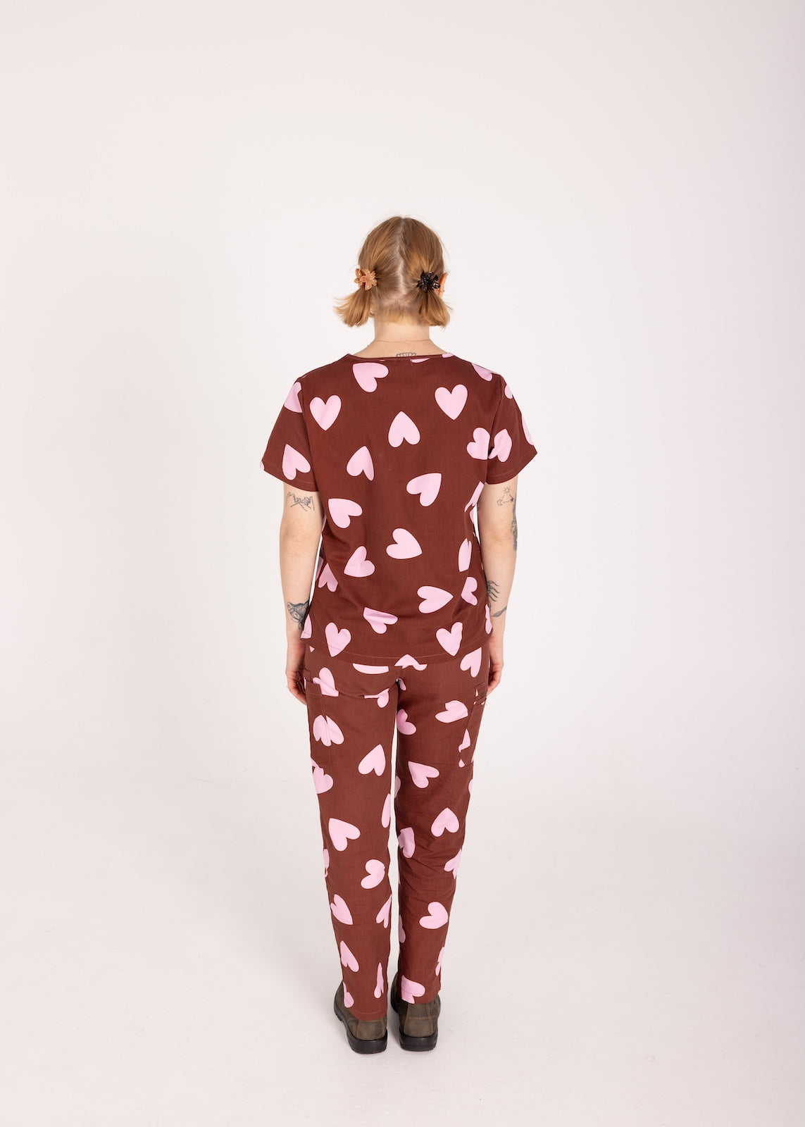 Woman wearing a brown fun scrubs with pink heart patterns on a plain background