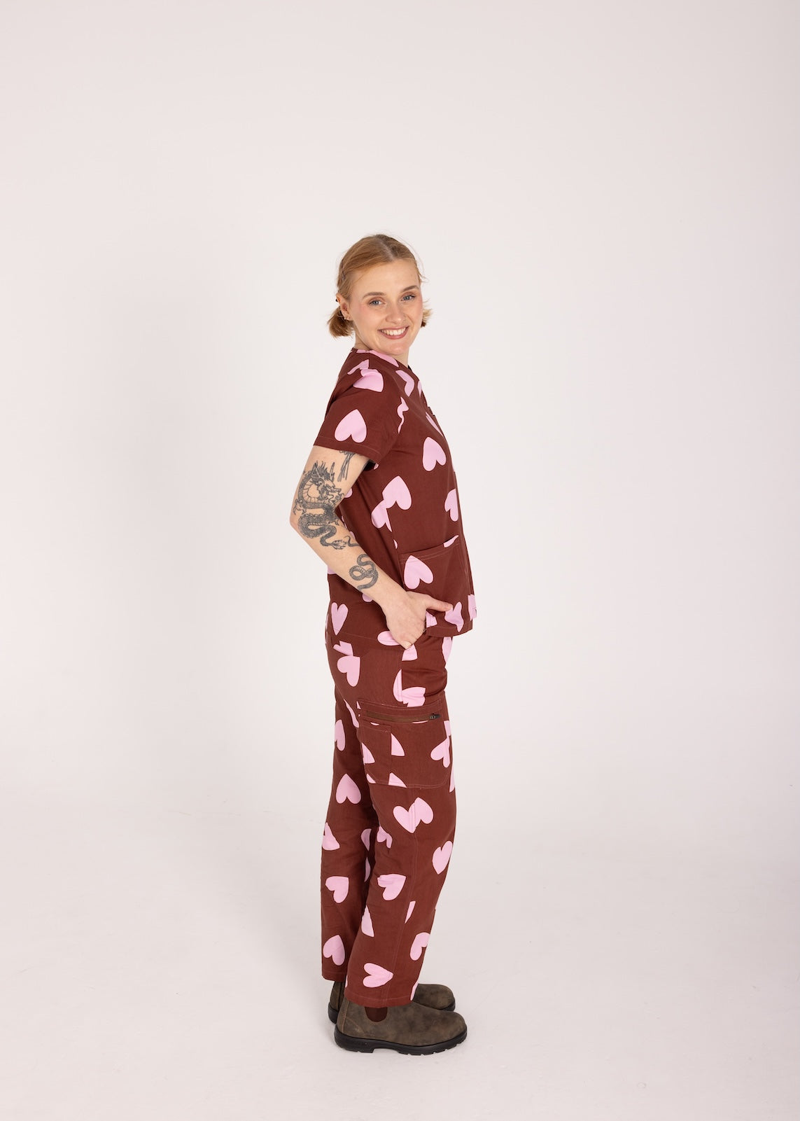 Woman wearing a brown fun scrubs with pink heart patterns on a plain background